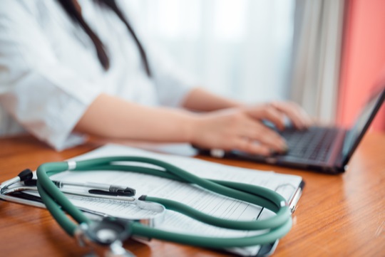 Стетоскоп на столе и врач за ноутбуком